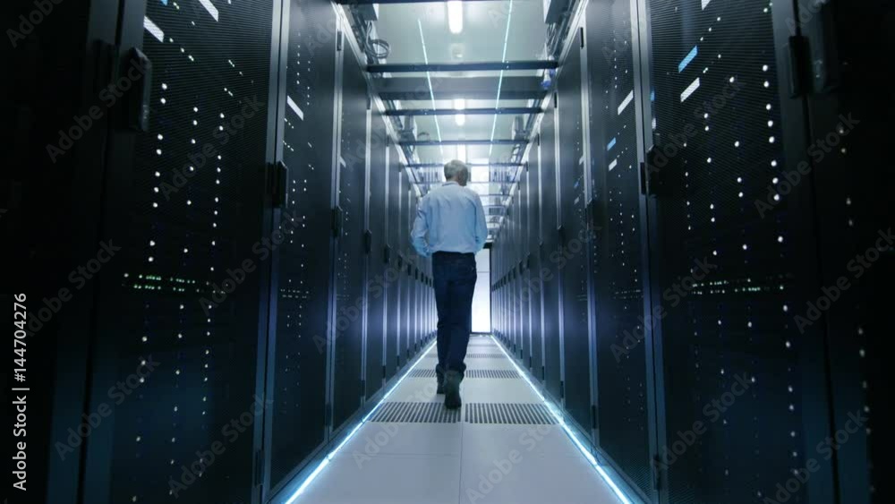 Poster server engineer in data center walks through sliding doors and opens server rack cabinet. shot on re