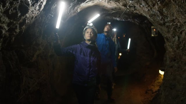  Team of potholers with hard hats and lamps exploring underground cave system.