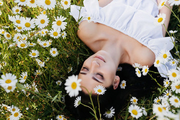 The beautiful woman in white dress lies in the field of chamomiles
