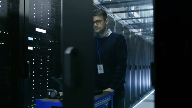 IT Technician in Data Center Pushes Crash Cart Through Sliding Doors. Rows of Working Rack Servers are Visible.  Shot on RED EPIC-W 8K Helium Cinema Camera.