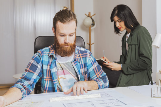 Man working with blueprint while woman writing