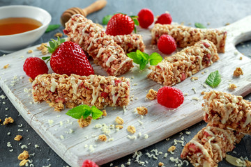 Granola bar with strawberries, raspberry honey and white chocolate on cutting board