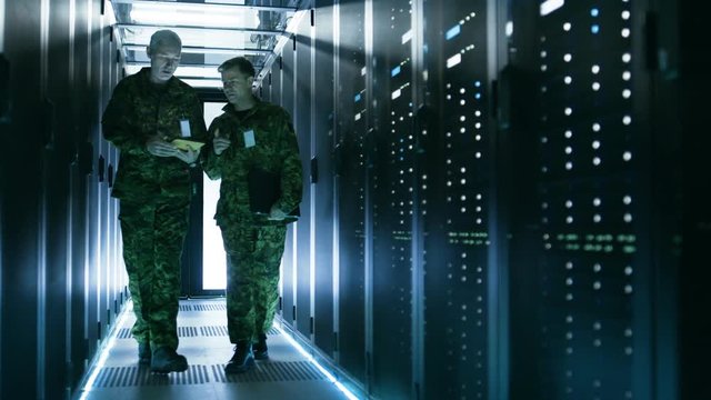 Two Military Men Walking in Data Center Corridor. One Uses Tablet Computer, They Have Discussion. Rows of Working Data Servers by their Sides.  Shot on RED EPIC-W 8K Helium Cinema Camera.
