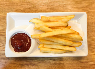 French fries in a bowl with tomato sauce on a wooden background