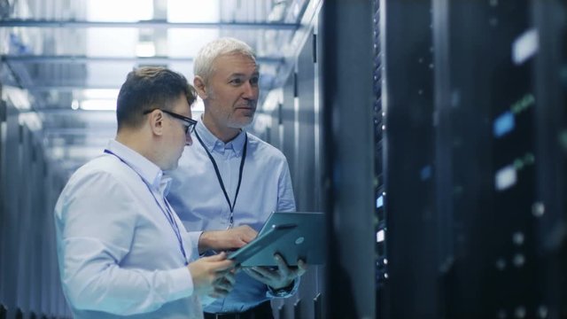 Two IT Technicians Standing in Data Center. They Use Laptop and Tablet Computer while Standing Beside Open Server Rack Cabinet.  Shot on RED EPIC-W 8K Helium Cinema Camera.