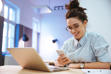 Cheerful student girl using mobile device in coworking space