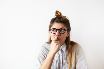 Close up portrait of funny confused woman in glasses thinking and looking aside standing on white...