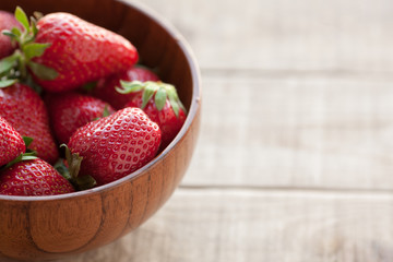 Fresh strawberries in a wooden bowl on a wooden table.