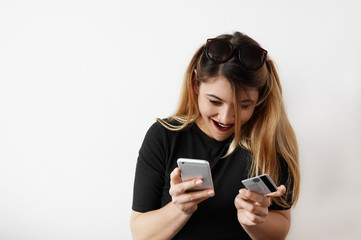 Fototapeta premium Happy young woman holding credit card using generic smart phone for shopping online. Pretty European female inspired by the upcoming shopping in her favorite online store. Technology and shopping