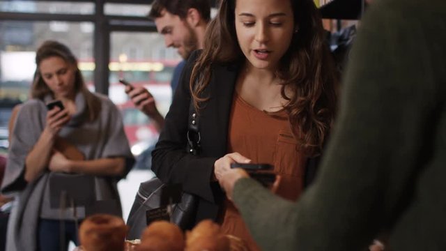  Customer in cafe makes payment with smartphone while queue of customers wait 