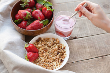 Healthy breakfast. Muesli and yogurt with strawberries. A woman's hand puts a spoonful of yogurt in the muesli