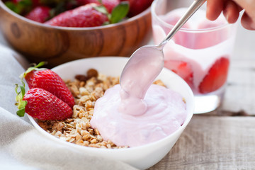 Healthy breakfast. Muesli and yogurt with strawberries. A woman's hand puts a spoonful of yogurt in...
