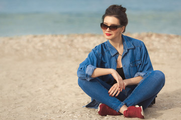 Fototapeta na wymiar Denim outfit fashion details. Relaxing stylish woman enjoying the sun with red glitter manicure in navy jeans holding sunglasses and leather small cross body bag.