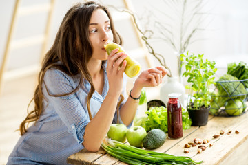 Beautiful woman sitting with healthy green food and drinking smoothie at home. Vegan meal and detox...