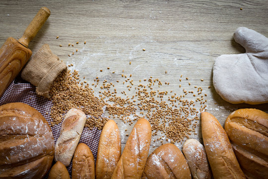 Bread border on wood with copy space background. Brown and white whole grain loaves still life composition with wheat flour sprinkled around. Bakery, cooking and grocery store concept.