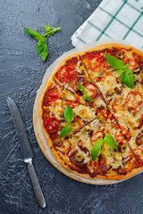 Traditional Italian pizza with tomato, cheese, salami, olives and basil on a dark stone background. Selective focus.Top view.