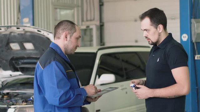 Mechanic showing a paper in a clipboard to a male client in a garage