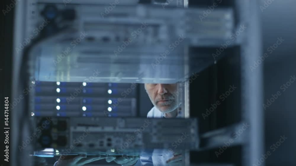 Poster two server technicians install hardware in server rack. they work in big modern data center. shot on