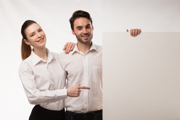 Young happy couple showing presentation pointing on placard over gray background