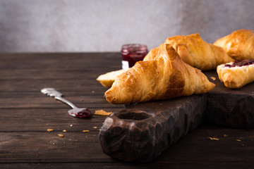Delicious fresh mini croissants with fruit jam on wooden cutting board on old dark background. Healthy Breakfast with copy space.
