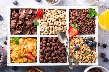 Variety of cold quick breakfast cereals with berries in white wooden box, healthy eating for kids, overhead shot