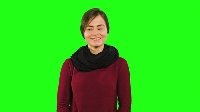 A young modest lady smiling and averting her eyes against a green background. Medium shot