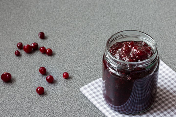 Cranberry jam in a glass jar on a grey background
