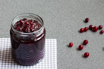 Cranberry jam in a glass jar on a grey background