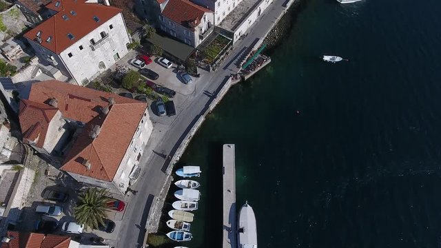 Flying above the old town of Perast. Ancient church, seaside promenade, marina with boats. Perast, Montenegro