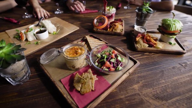 Close up shot of a wooden table with vegetarian snacks that are beautifully decorated and served by the waiter. Different vegetables lie in plates, sauces in bowls