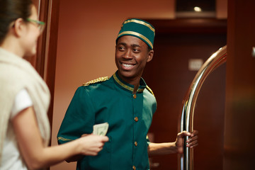Young guest of hotel giving porter money for his help