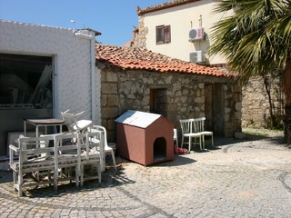 Alte Tische und Stühle mit Hundehütte im Sommer vor dem alten Haus aus Bruchstein und Naturstein...