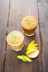 two smoothie of apples, pears, oranges, bananas, standing on a wooden covering