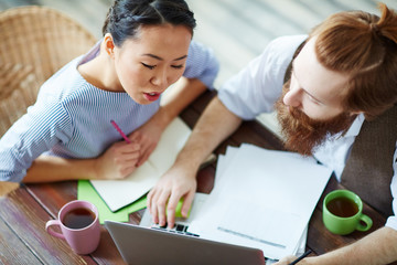 Young woman looking at laptop display while discussing data with colleague