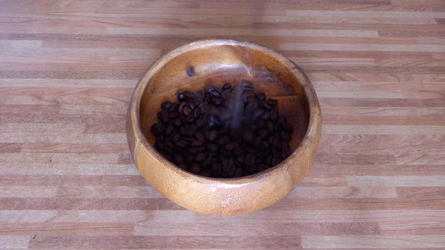 Roasted coffe beans falling in wooden bowl on brown table. Food or cooking theme. With orginal sound of grains drop.