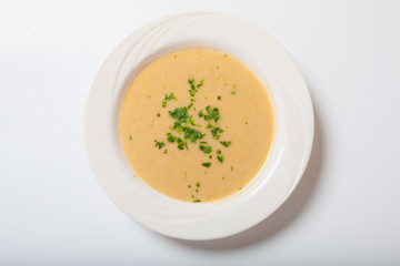 Creamy vegetables soup with fresh herbs in a white bowl