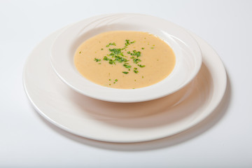 Creamy vegetables soup with fresh herbs in a white bowl