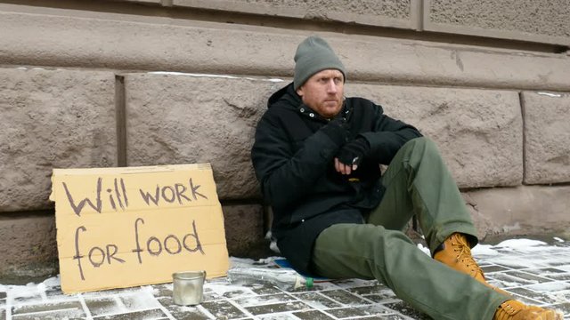 Frozen homeless man warming hands. Sign on cardboard - will work for food.