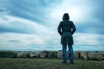 Lonely hooded female person from behind standing at seashore