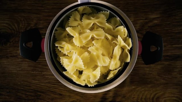 The farfalle paste is shaken in a colander over a pot standing on a table. Slow motion, top view