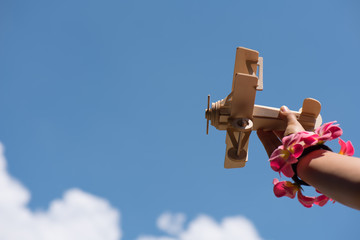 Girl holding toy wood plane at an airshow with crowd in the background and blue sky - obrazy, fototapety, plakaty