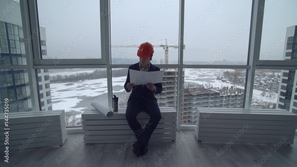 Poster worker holding blueprint with floor map. architect wearing elegant suit and helmet sitting at constr