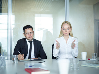 Portrait of two business people in meeting: man and woman sitting at table in conference room while woman explaining idea gesturing actively