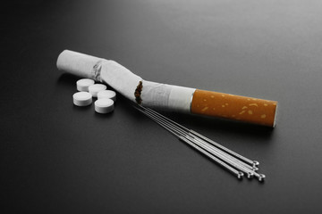 Cigarette with needles and pills on table