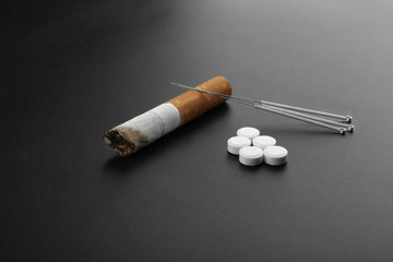 Cigarette with needles and pills on table