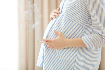 Pregnant woman smoking cigarette in light room, closeup