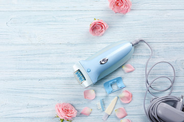 Modern epilator with accessories and flowers on wooden background