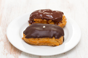 choclate eclairs on white dish on wooden background