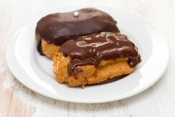 choclate eclairs on white dish on wooden background