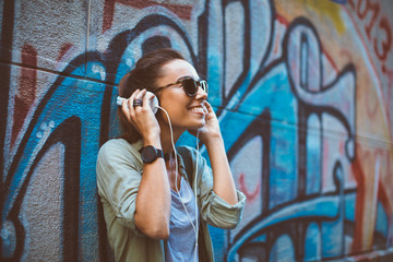 Young woman listening to music via headphones on the street - obrazy, fototapety, plakaty
